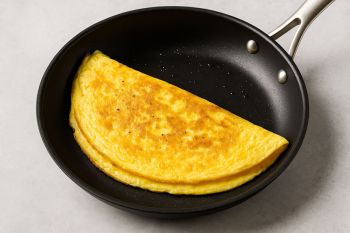 Αφράτη ομελέτα σε αντικολλητικό τηγάνι, χρυσαφένια και ζουμερή, έτοιμη για σερβίρισμα