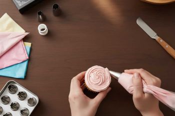 Επαγγελματική διακόσμηση cupcake με μύτη κορνέ αστεριού. Κοντινό πλάνο σε χέρι ζαχαροπλάστη που χρησιμοποιεί σακούλα ζαχαροπλαστικής και coupler. - CookPro