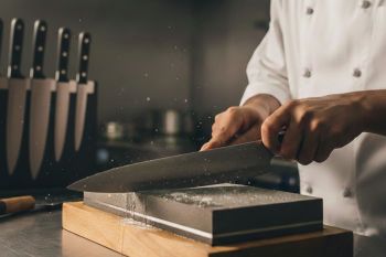 Επαγγελματίας σεφ ακονίζει μαχαίρι κουζίνας πάνω σε πέτρα ακονίσματος σε επαγγελματική κουζίνα - Cookpro How-To